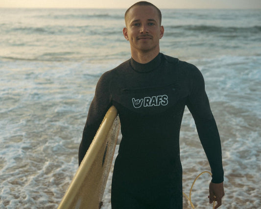 Man in a wetsuit holding a surfboard on a beach